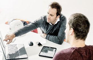 Foto zwei Mitarbeiter vor Laptop und Ipad 