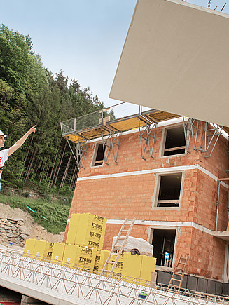 Betonbaulehrling dirigiert eine Betonplatte an einem Kran