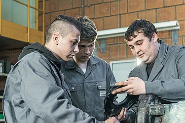 Foto drei junge Männer betrachten ein Metallteil