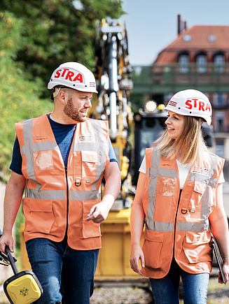 Foto 2 Bauarbeiter auf Gleisbaustelle, Bagger im Hintergrund