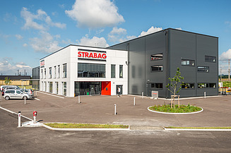 Foto eines Lehrlings mit Blick in Kamera, im Hintergrund weitere Lehrlinge beim Pflastern