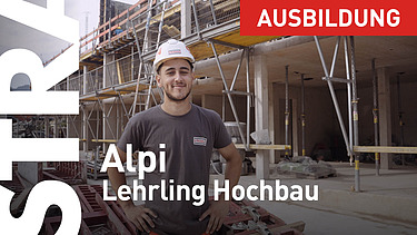 Lehrling im Hochbau steht mit Helm vor einem Gerüst.