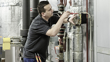 Lehre Kälteanlagentechniker:in Bild 1 Foto Mitarbeiter arbeitet an Rohrleitungsanlage