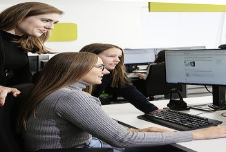 Foto drei Mitarbeiterinnen blicken auf zwei Bildschirme