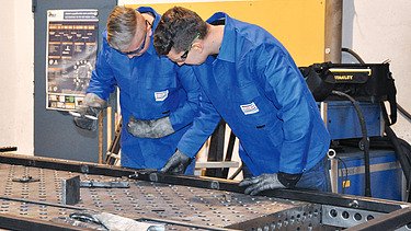 Foto zwei Mitarbeiter beim Bearbeiten eines Metallrahmens
