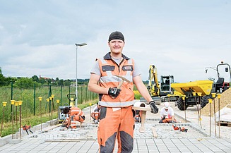 Pflasterer steht vor zu pflasternder Fläche in Arbeitskleidung.