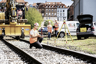 Foto Bauarbeiter kniet auf Gleisen, 2 Mitarbeitende im Hintergrund