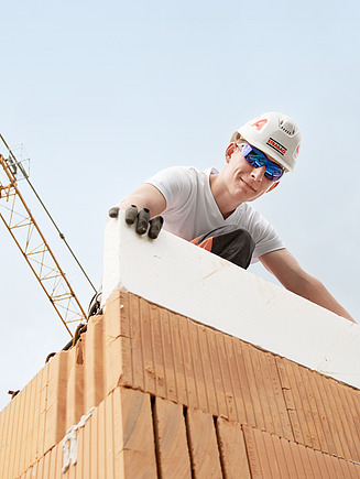 Ein Lehrling setzt einen Mauerstein auf eine gemauerte Wand