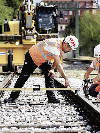 Foto drei Bauarbeiter prüfen die Höhe eines Gleises mit der Wasserwaage
