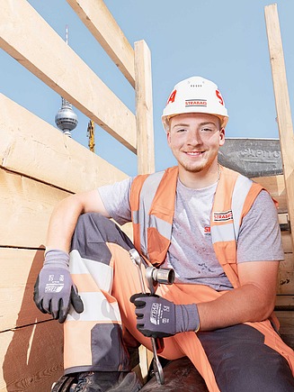 Bauarbeiter bedient Baufahrzeug welches Erde auskippt.