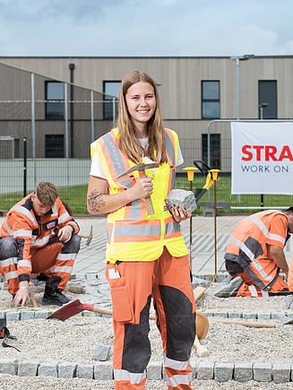 Foto von Lherling auf der Baustelle mit Blick in die Kamera, im Hintergrund weitere Lehrlinge