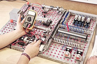 Foto zwei Hände, elektronisches Messgerät und Schaltungsplatte