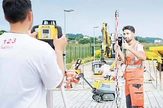 Lehrling steht mit Tablet auf einer Baustelle. 
