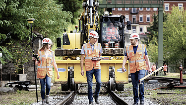 Foto drei Mitarbeitende mit Arbeitsgerät in der Hand schreiten über Gleisee