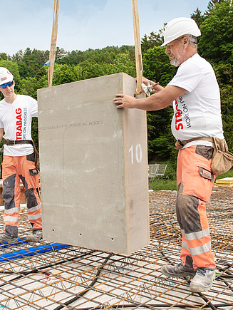Zwei Betonbauer bewegen eine am Kran hängende Betonplatte