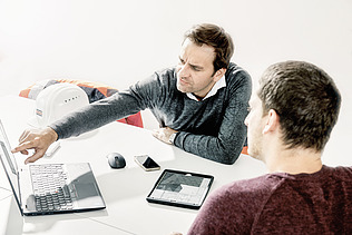 Foto zwei Mitarbeiter vor Laptop und Ipad 