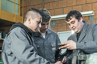 Foto drei junge Mitarbeiter beim Betrachten eines Metallteiles