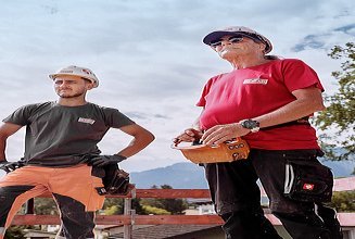 2 STRABAG  Mitarbeiter und einen volle Bagger-Schaufel auf einer Baustelle.