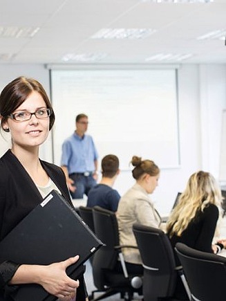 Foto Mitarbeiterin mit Laptop in der Hand vor Mitarbeitergruppe im Besprechungszimmer