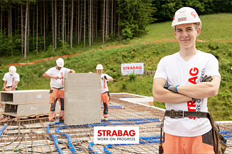Lehrling bei STRABAG auf einer Baustelle mit Kollegen im Hintergrund.